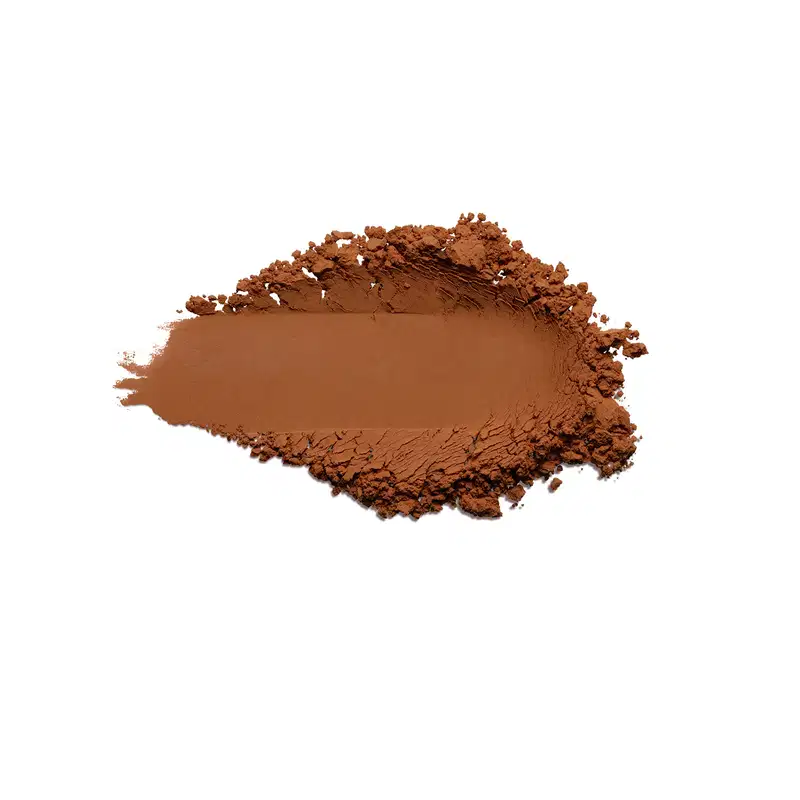 Pó compacto de cor 5 marrom terrosa vibrante. O produto apresenta uma textura fina e pulverizada, formando uma superfície irregular com pequenos montes de pó solto ao redor de uma área central mais compactada.