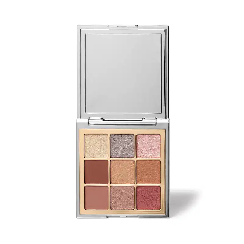 Paleta de sombras de olhos compacta com espelho integrado. Embalagem retangular de metal cromado. Nove sombras prensadas em tons neutros e rosados, variando de bege claro a marrom terroso e rosa envelhecido. Superfície das sombras com acabamento dourado.