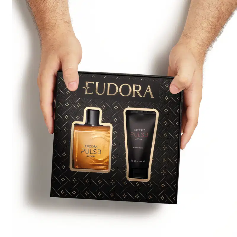 Caixa preta com o logotipo EUDORA e padrão geométrico repetido em dourado. Na sua parte frontal há a imagem do frasco de Eudora Pulse Action e do tubo do balm pós-barba.A caixa é vista de cima e é segurada pelos lados por duas mãos masculinas brancas.