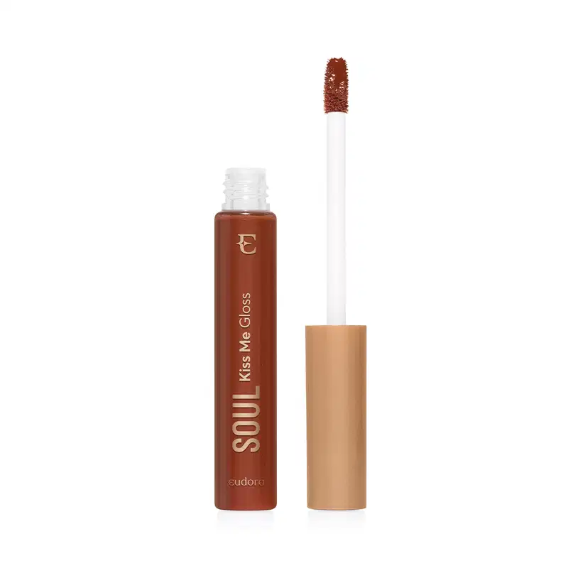 Frasco de vidro transparente contendo gloss marrom caramelo achocolatado. Rótulo com o nome do produto e da marca em letras douradas sobre fundo transparente do frasco e marrom do produto. Aplicador de espuma em formato de pincel firme. Tampa dourada