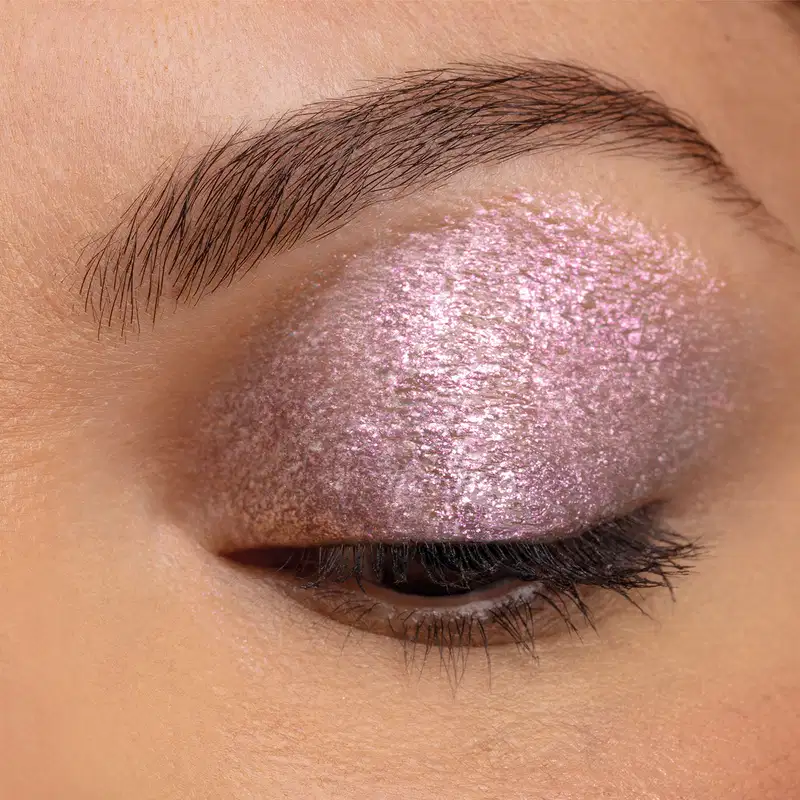 Destaque para o olho da modelo indicando o uso do produto Glitter Glam Paetê nas pálpebras. Tem um efeito rosado e partículas brilhantes.