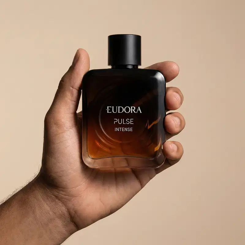 Imagem de um frasco do desodorante colônia da marca Eudora Pulse Intense, em um fundo bege claro. O produto é segurado por uma mão masculina.
