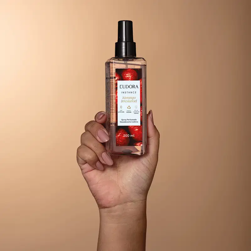 O produto mostrado é um spray perfumado da marca Eudora, da linha Instance Morango. O frasco é transparente com um borrifador preto e um rótulo vermelho e branco. A embalagem possui informações sobre o produto, como o volume de 200 ml.