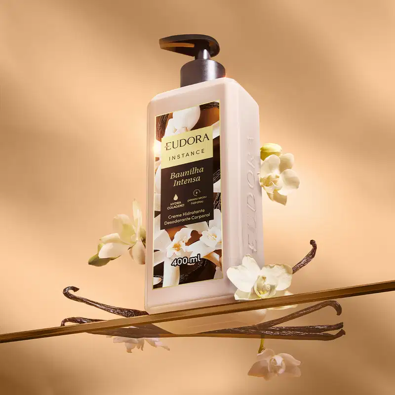 Embalagem do creme hidratante Eudora Instance rodeado por flores e varas de baunilha, em um cenário com tons quentes e neutros, sugerindo um contexto de cuidados corporais e fragrância.