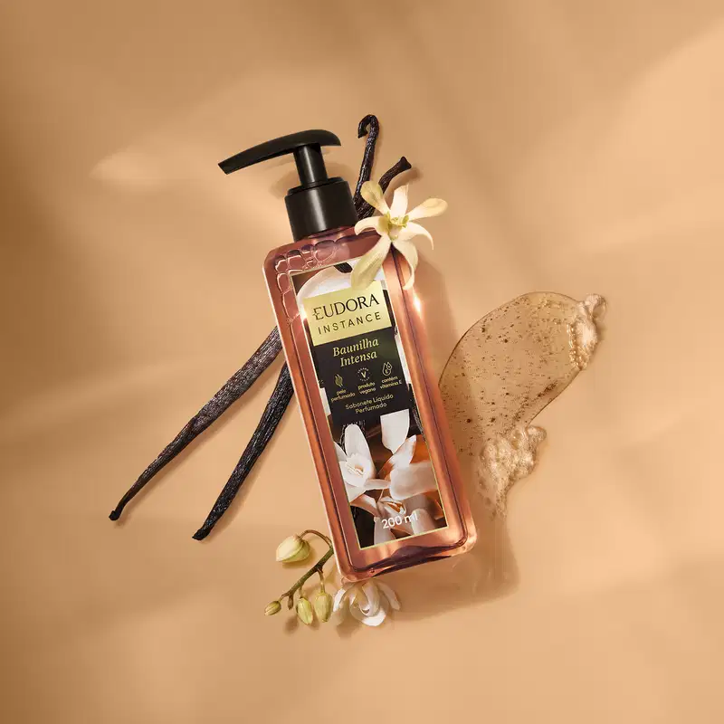 Ambiente de beleza com produto sabonete líquido da marca Eudora, embalagem com design elegante e flor de baunilha, em cenário com tons terrosos, sugerindo um contexto de cuidados pessoais e relaxamento.