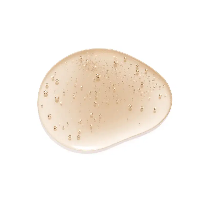 A superfície do produto apresenta uma textura suave e cremosa, com uma tonalidade bege clara e uma aparência levemente brilhante, com pequenas bolhas dispersas por toda a superfície, sugerindo uma consistência leve.
