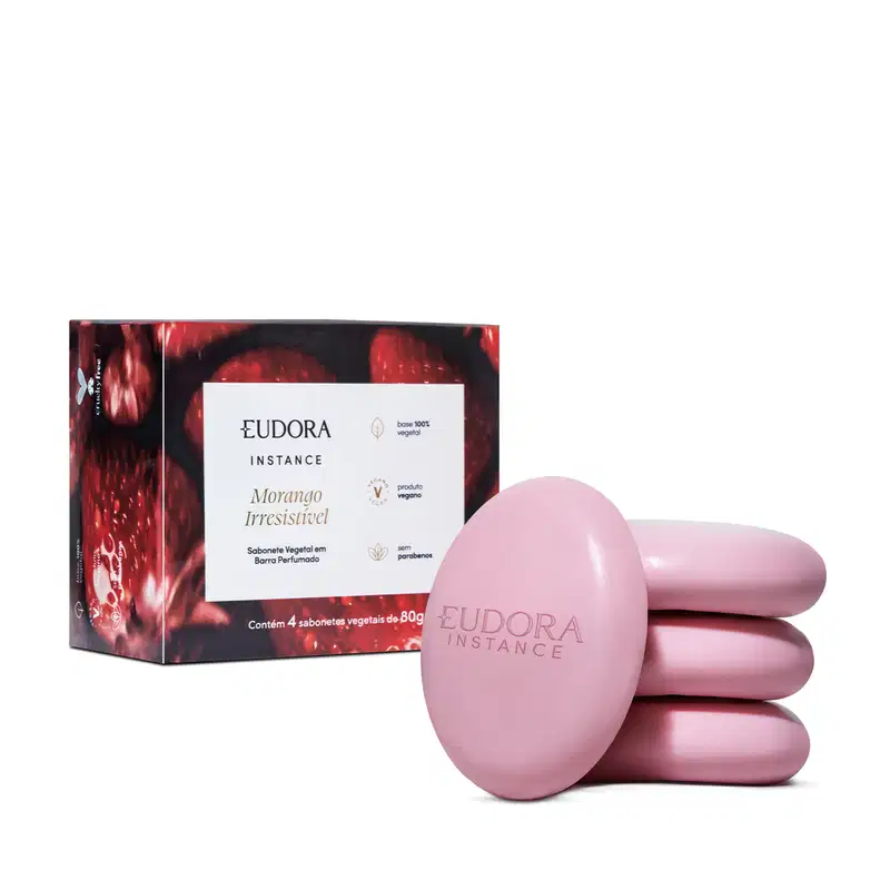 O produto apresentado é um conjunto de sabonetes vegetais da marca Eudora Instance, com fragrância de morango irresistível. A embalagem consiste em uma caixa vermelha e preta, contendo 4 sabonetes em formato oval de cor rosa.