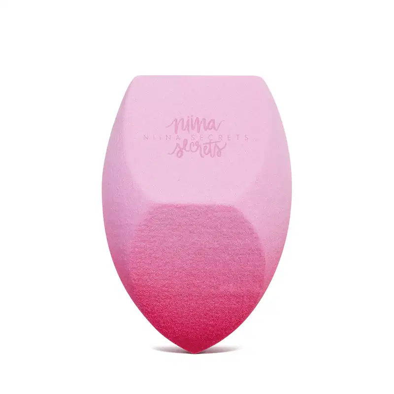 O produto apresentado é uma esponja para maquiagem da marca Niina Secrets, com uma coloração degradê de rosa claro a rosa escuro. Possui um formato arredondado e achatado em diferentes partes.