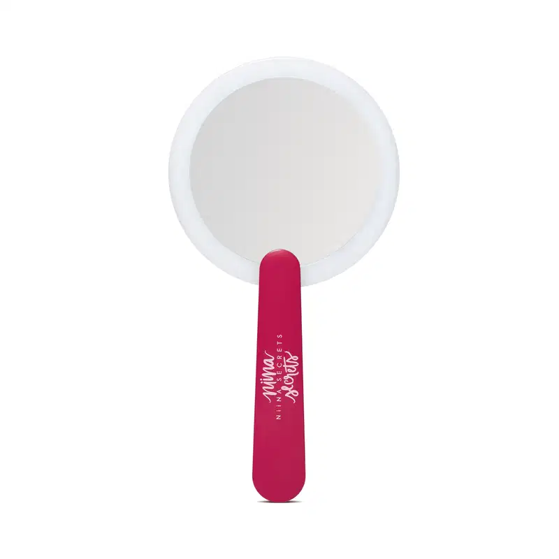 O produto apresentado é um espelho de mão da marca Niina Secrets. Possui um formato circular com um acabamento branco. O cabo do espelho é de cor rosa vibrante, com o nome da marca impresso em letras brancas.