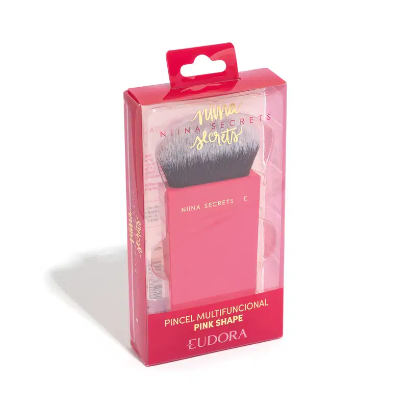 O produto apresentado é um pincel de maquiagem da marca Niina Secrets. O pincel possui cerdas macias e uma base em um tom rosa vibrante, com o nome da marca impresso em letras douradas. Na imagem, está dentro da embalagem de plástico e transparente.