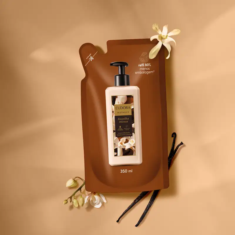 Ambiente de beleza com embalagem de produto Eudora Instância, contendo baunilha intensa, em fundo bege com flores brancas e vagens de baunilha, sugerindo um contexto de cuidados pessoais e fragrância natural.