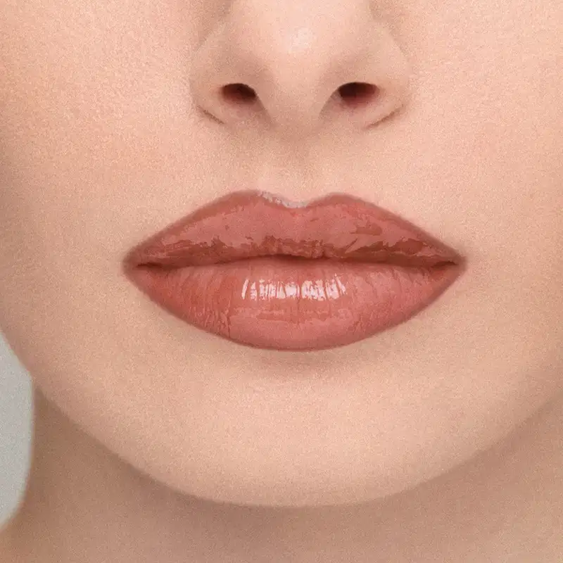 Imagem em close-up de lábios de uma modelo, mostrando o efeito do Gloss Labial: Lábios amarronzado com brilho, em primeiro plano, sobre fundo neutro.
