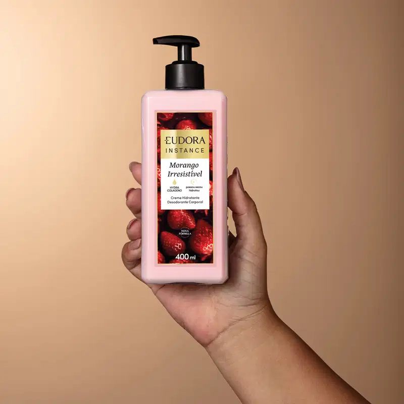 Frasco de creme hidratante corporal da marca Eudora Instance, com rótulo vermelho e rosa destacando o aroma de morango irresistível, com capacidade de 400 ml e bomba de pressão preta.