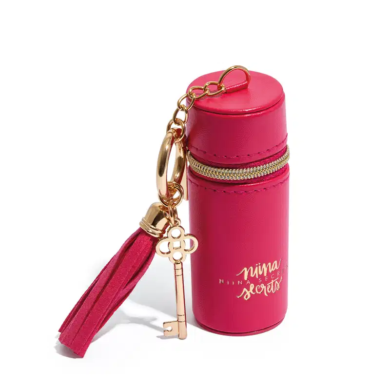 Acessório rosa em formato cilíndrico com zíper dourado, pingente em formato de chave e texto "Niina Secrets" impresso na embalagem.