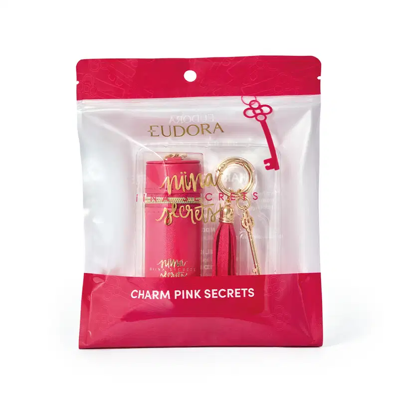 Embalagem rosa com detalhes dourados contendo um acessório da marca Niina Secrets, com pingente e borla decorativa.