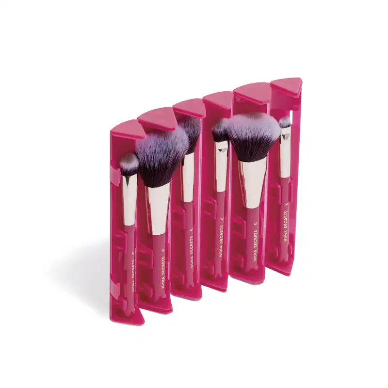 Seis pincéis de maquiagem Niina Secrets com cerdas pretas/cinzas e cabos dourados e rosa, embalados em estojos rosa pink com abas triangulares.