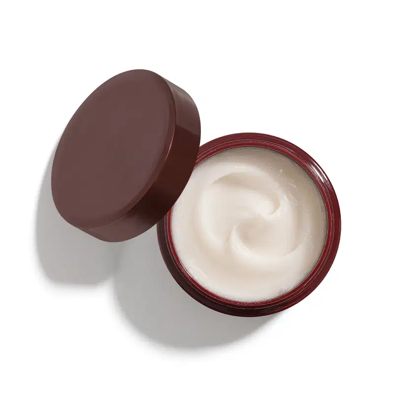 Recipiente de plástico vinho escuro contendo creme branco e cremoso, com superfície lisa e brilhante, sugerindo uma textura suave e hidratante.