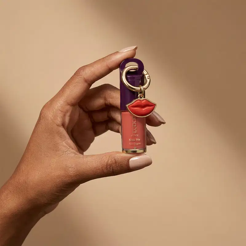 Batom com chaveiro da linha Kiss Me da Eudora, com embalagem roxa e detalhes dourados, exibindo o nome do produto em destaque.