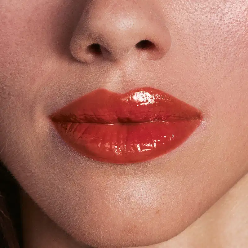 Imagem de close-up de lábios femininos com batom vermelho brilhante, sugerindo um produto de maquiagem de alta qualidade e acabamento luxuoso.