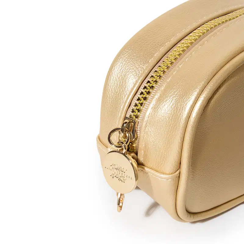 Imagem angulada da bolsa dourada com zíper e pingente redondo. A bolsa possui uma superfície lisa e brilhante, com detalhes em dourado, incluindo o zíper e o pingente. Trata-se de um item de design elegante e sofisticado.