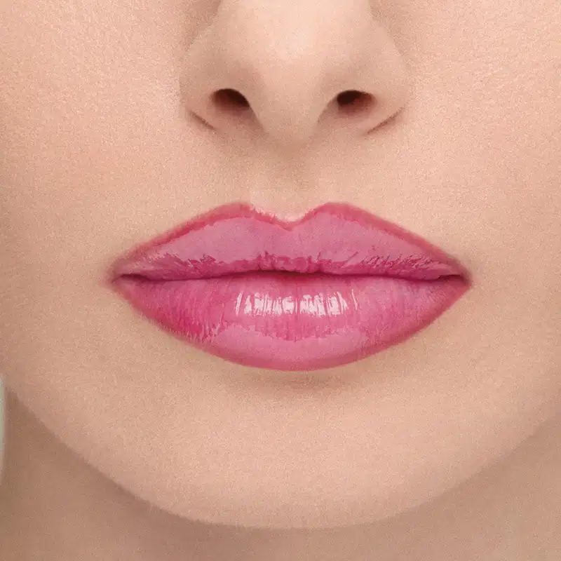 Imagem em close-up dos lábios de uma modelo, mostrando o efeito do Gloss: Lábios rosados com brilho, em primeiro plano, sobre fundo neutro.
