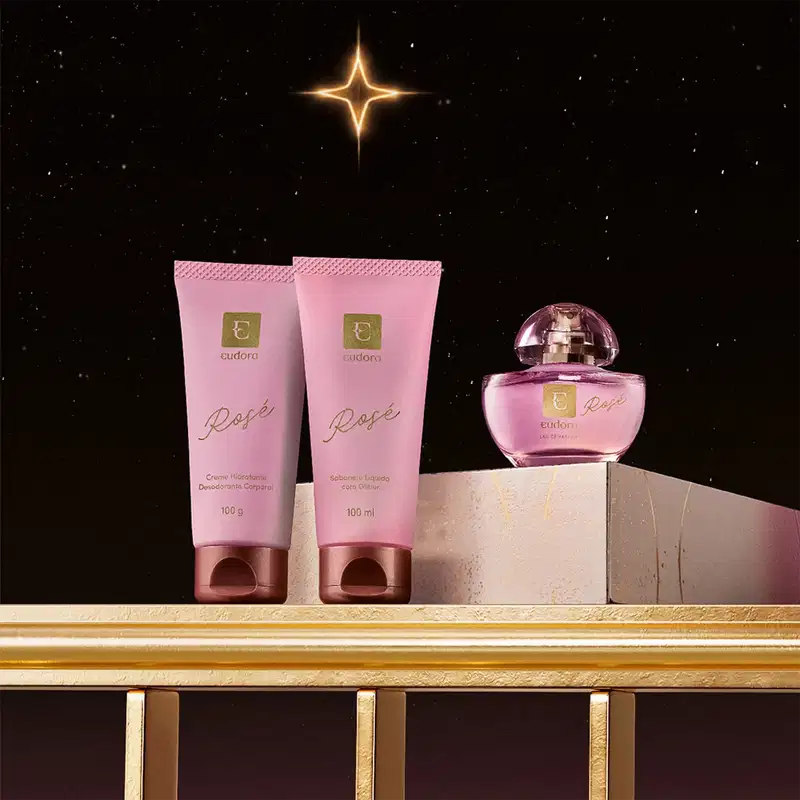 Linha Rosé Eudora composta por dois tubos rosa de 100g e 100ml com detalhes em ouro, e frasco de perfume rosa com tampa espelhada. Embalagem elegante com logotipo Eudora em dourado.
