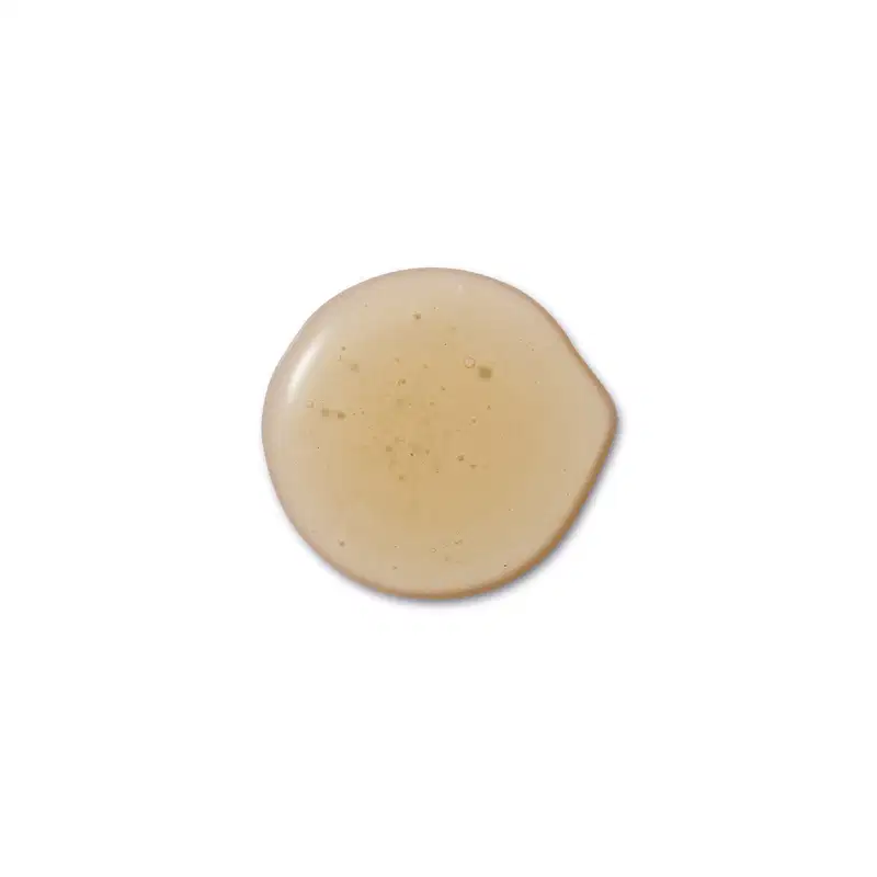 Textura cremosa com consistência densa e uniforme. Cor bege claro com pequenas partículas visíveis dispersas. Acabamento com brilho suave e aspecto liso. Estrutura compacta e homogênea, típica de base ou corretivo em pó comprimido.