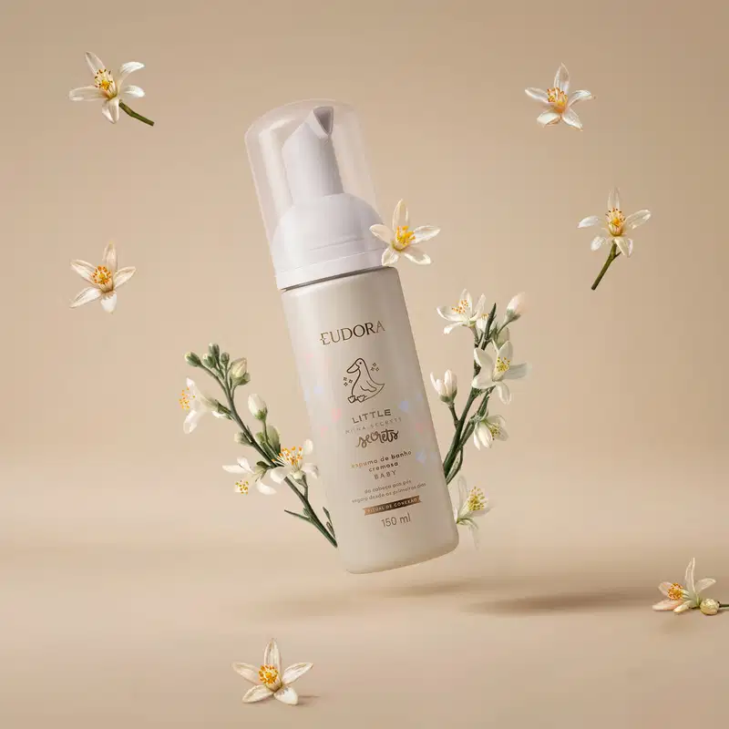 Ambiente de beleza minimalista e natural, com flores brancas delicadas em fundo bege, destacando o produto Eudora Little Secrets, uma espuma de banho com design elegante e moderno.