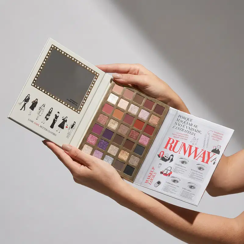 Paleta de sombras de olhos com 35 tons variados, embalada em uma caixa com ilustrações de moda. Revista de moda "Runway" de O Diabo Veste Prada aberta em três lados, exibindo informações sobre tendências e estilos.