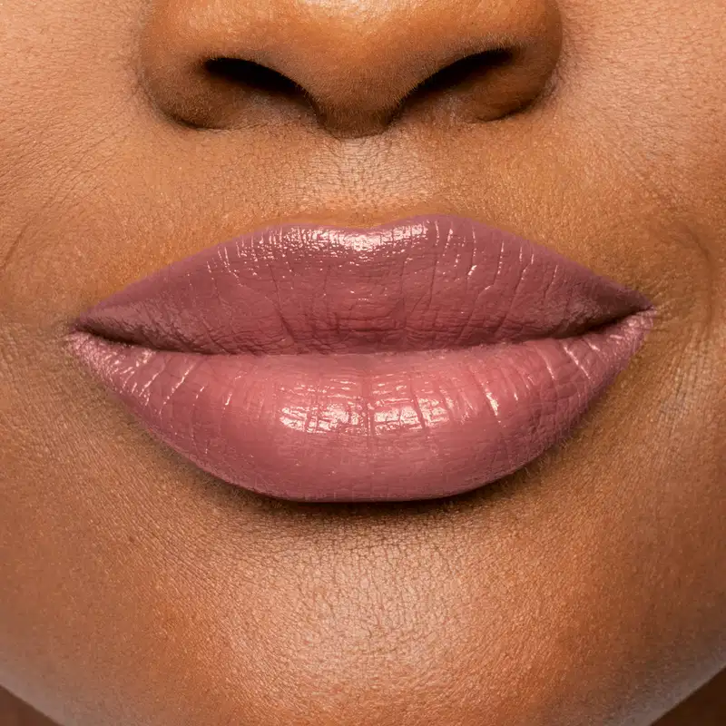 Imagem com foco nos lábios femininos com batom caramelo, com um acabamento lustroso e brilhante. O foco está nos lábios, que ocupam a maior parte da imagem.
