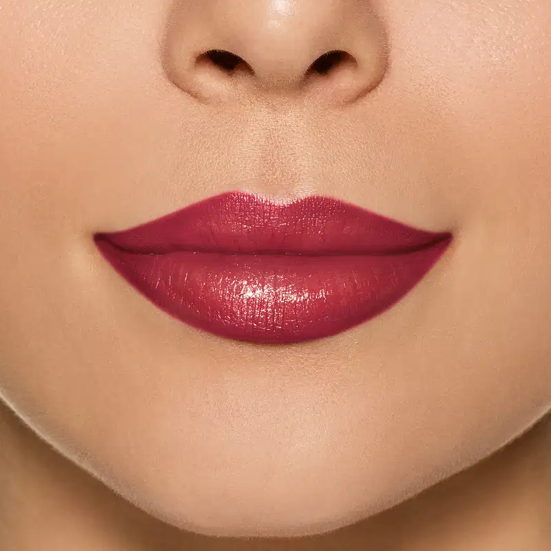 Imagem com foco nos lábios femininos com batom vermelho cereja, com um acabamento lustroso e brilhante. O foco está nos lábios, que ocupam a maior parte da imagem.
