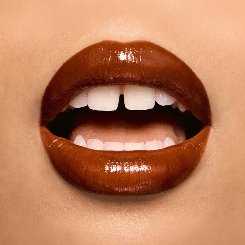 Imagem em close de lábios com batom canela em tom brilhante e glossy em primeiro plano.
