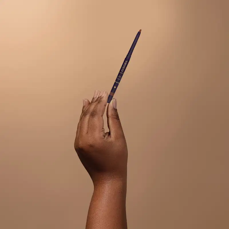 Mão segurando uma lapiseira labial da marca Eudora sobre fundo bege.