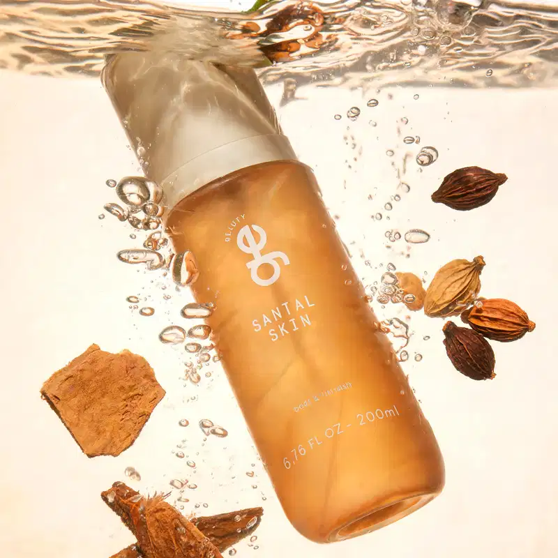 Frasco âmbar translúcido de 200ml da GE Beauty, "Santal Skin", tampa branca, submerso em água com cardamomo e sândalo. Rótulo branco.