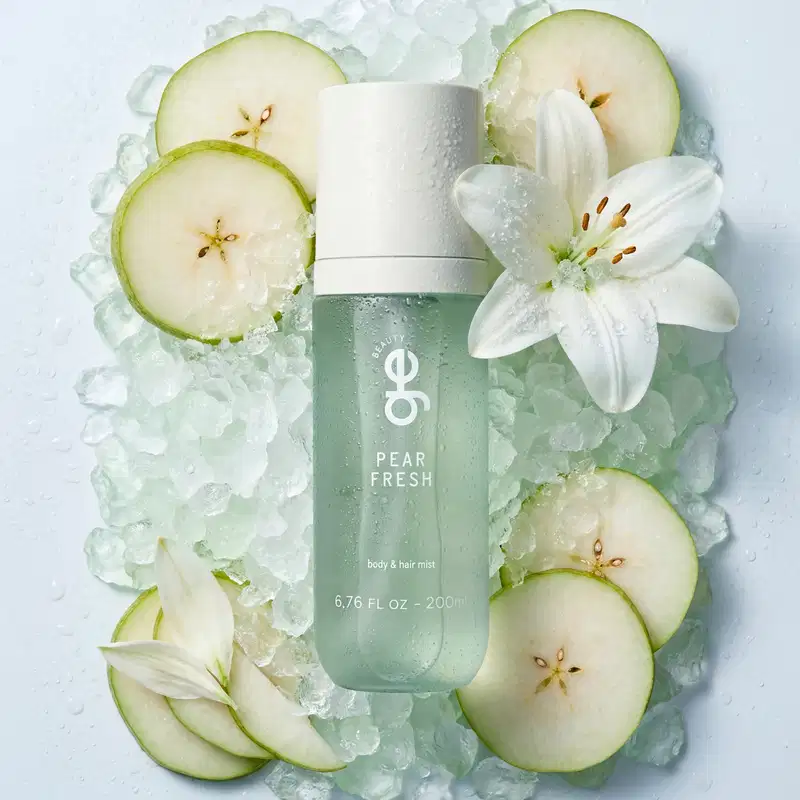 Spray corporal e capilar GE Beauty "Pear Fresh", frasco de 200 ml na cor verde-menta translúcida com tampa branca. Cercado por gelo, fatias de pera e uma flor de lírio branca.