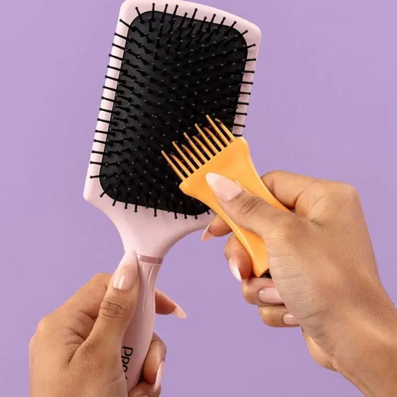 A imagem mostra uma mão feminina segurando uma escova e outra utilizando o limpador de escovas nas cerdas.