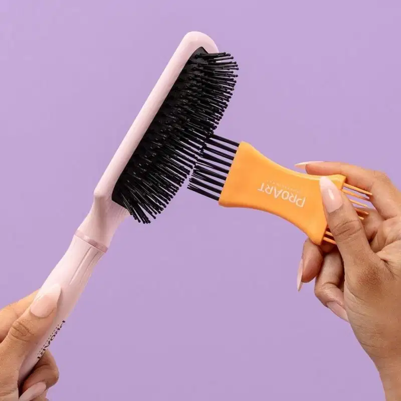 A imagem mostra uma mão feminina segurando uma escova e outra utilizando o limpador de escovas nas cerdas.