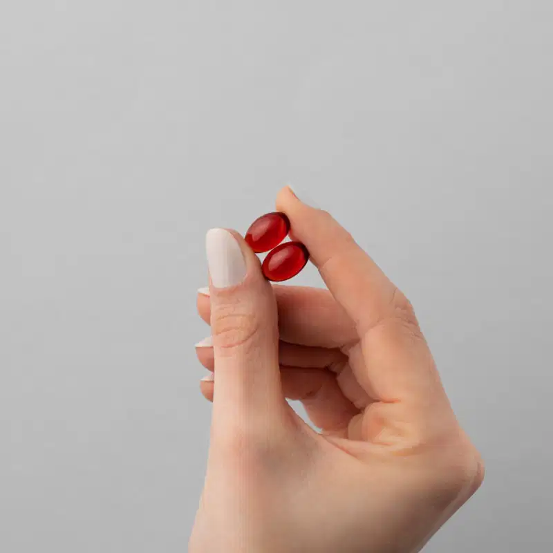 A imagem mostra uma mão segurando duas cápsulas com o dedo polegar e o indicador.