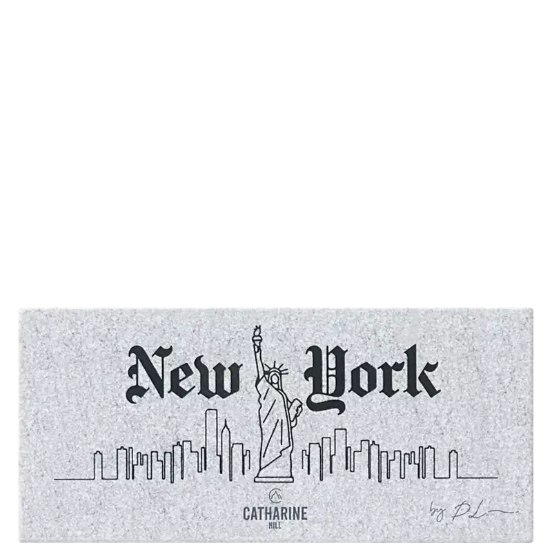 A embalagem fechada mostra a imagem em preto e branco que apresenta o logotipo e o nome "New York" em um estilo de fonte gótica antiga. A imagem inclui um desenho da Estátua da Liberdade e um esboço da skyline de Nova York com vários edifícios.