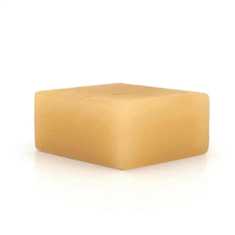 O produto apresentado é um bloco de sabonete de cor bege, um sólido retangular com superfície lisa e uniforme.