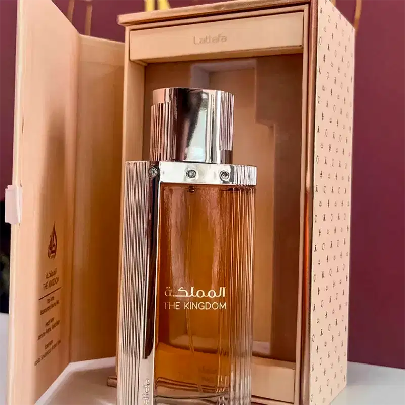 Frasco de perfume Lattafa Perfumes "The Kingdom" em embalagem de madeira com detalhes em dourado e prata. O frasco possui formato retangular com linhas verticais e tampa metálica.