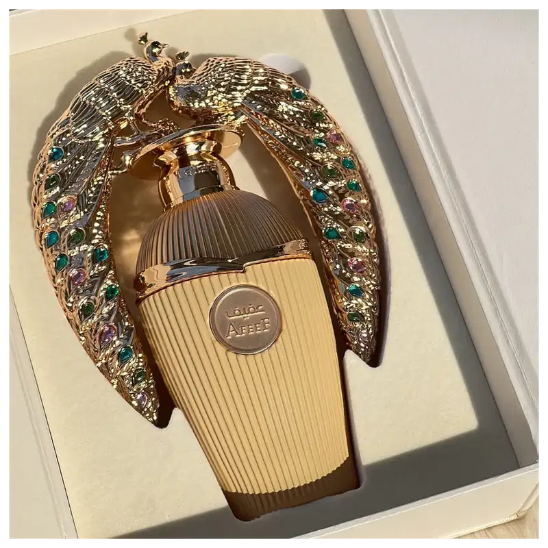 Frasco de perfume dourado da marca Lattafa Perfumes, com detalhes em formato de pássaro ornamentado com pedras coloridas, embalado em uma estrutura decorativa.