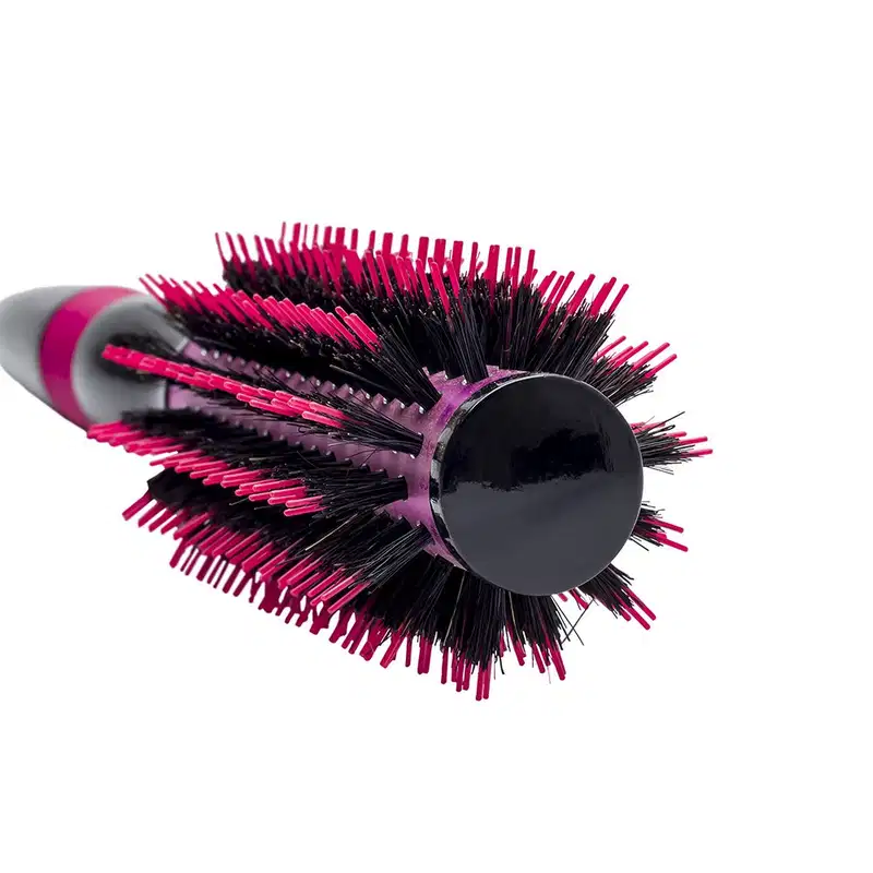 A imagem mostra a escova de cabelo em formato arredondado. Ela possui um corpo preto com cerdas rígidas e densas em tons de rosa vibrante e preto. Design moderno e ergonômico com cabo emborrachado rosa.