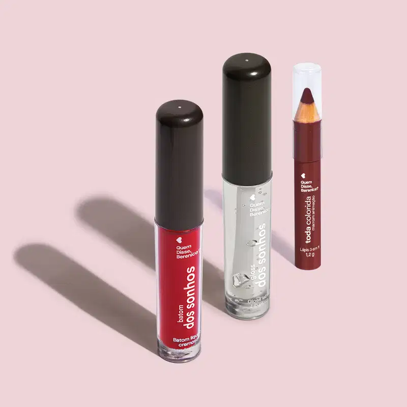 Frasco transparente com líquido vermelho de Batom dos Sonhos, frasco transparente com líquido claro e tampa preta de gloss labial incolor Batom dos Sonhos e lápis 3 em 1 Toda Colorida Marrom Animação, todos da marca Quem Disse, Berenice? em fundo lilás.