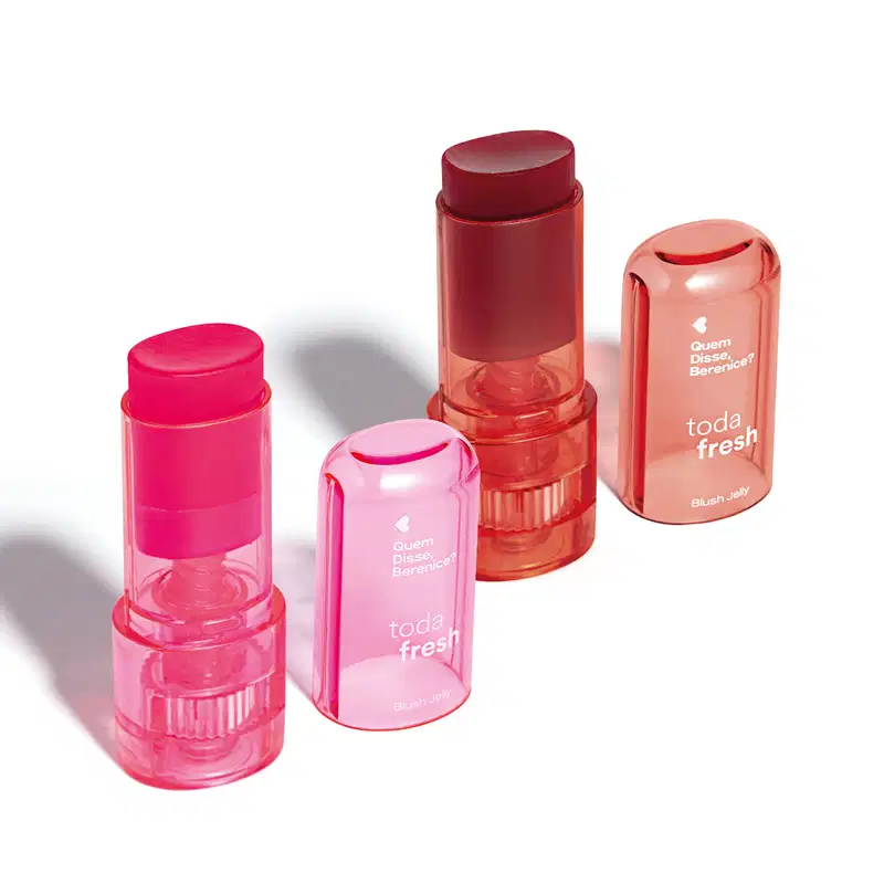 Produtos de maquiagem da marca Quem Disse, Berenice? em embalagens plásticas translúcidas nas cores rosa e vermelho, incluindo um batom, um blush em bastão e um produto de acabamento.