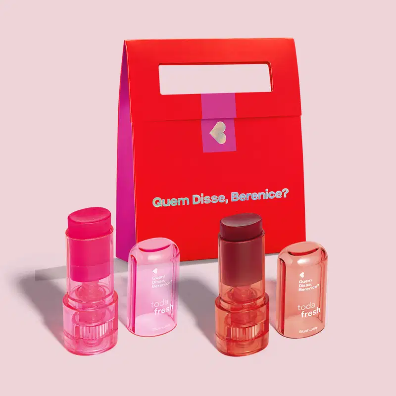 Caixa vermelha e rosa com produtos de maquiagem da marca Quem Disse, Berenice?, incluindo batons, blush e outros itens de beleza em embalagens coloridas e com textos promocionais.