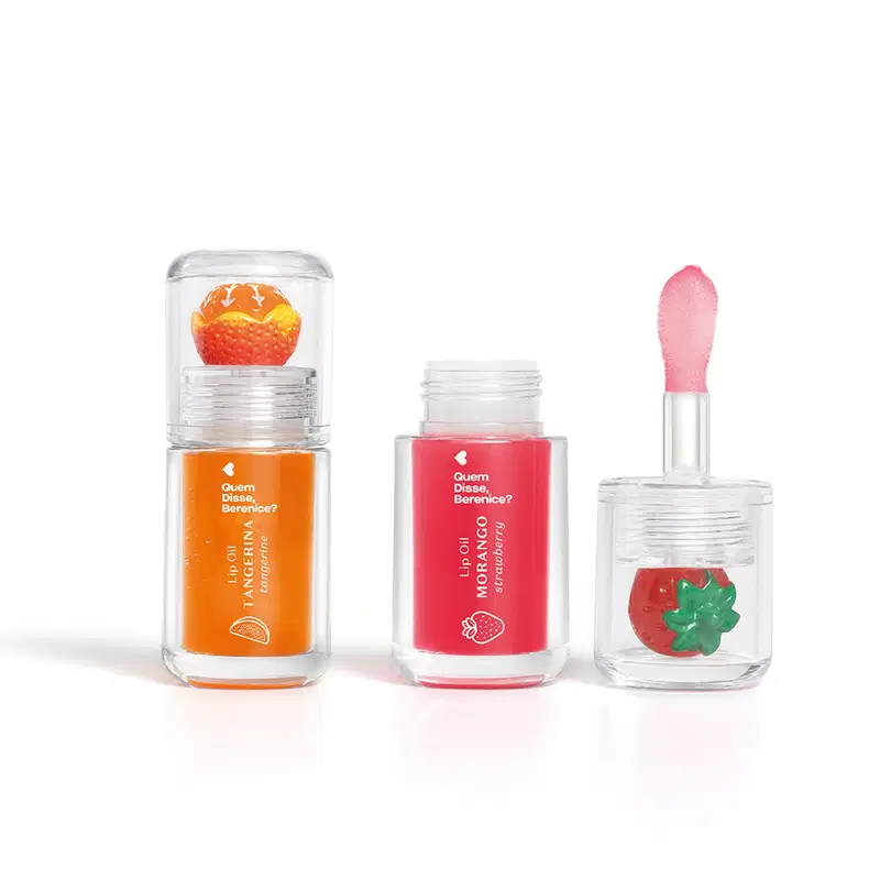 Imagem do Combo Lip Oil Quem Disse Berenice? com um produto na cor Vermelho Morango, em tonalidade vermelha e morango decorando a tampa e e outro na cor Coral Tangerina em tonalidade laranja com uma tangerina de decoração. As embalagens são transparentes.