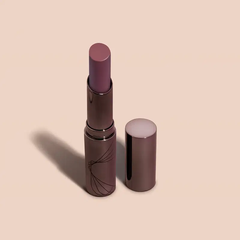 Batom semi matte de cor vinho escuro em embalagem cilíndrica marrom escura com detalhes pretos da marca Volumão Vinho Castanhelê Quem Disse, Berenice? em fundo lilás.