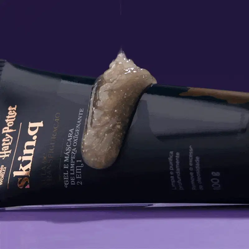 Bisnaga azul-marinho com letras na cor dourada e branca de gel e máscara de limpeza Borbulhante 2 em1 Skin q. Quem Disse Berenice? Harry Potter em fundo verde escuro e superfície azul com líquido brilhante caindo sobre a embalagem.