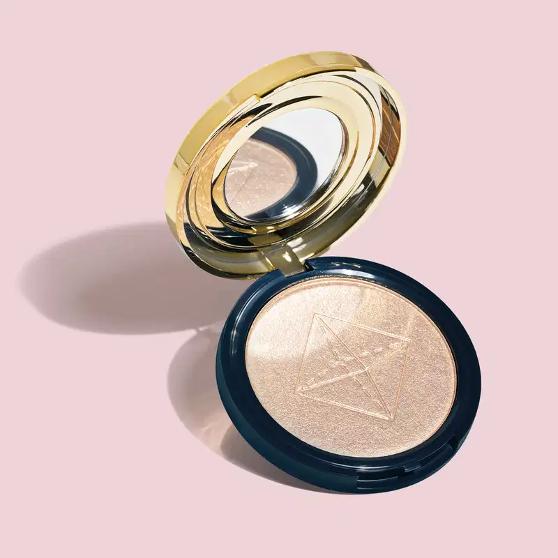 Produto de maquiagem em pó compacto com acabamento iluminado. Embalagem redonda azul com tampa dourada espelhada em camadas concêntricas. O pó compacto apresenta um acabamento perolado dourado. O design da embalagem dourado luxuoso contrasta com o azul.